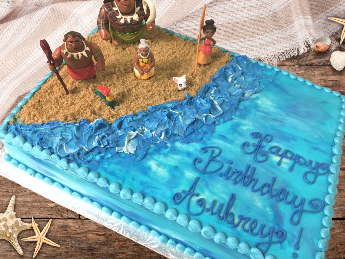 A Moana Sheet cake with moana cake toppers, with brown sugar sand and blue buttercream.