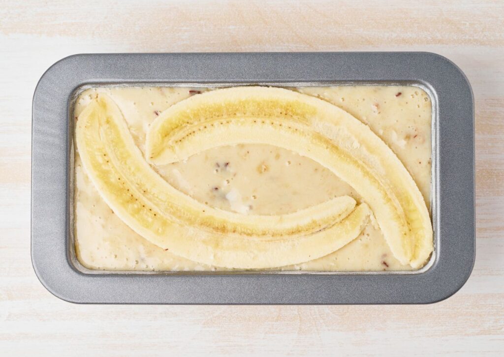 Banana bread batter in a loaf pan with bananas on top.