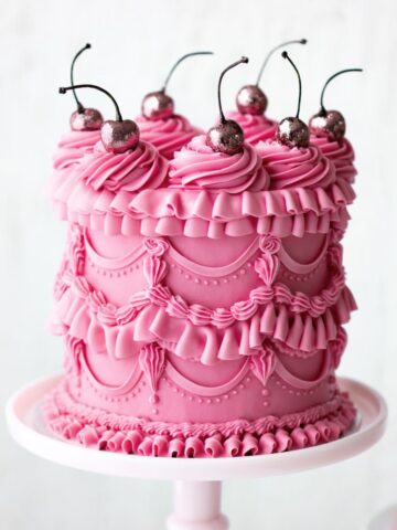 A decorated cake with piped details and cherries on top.