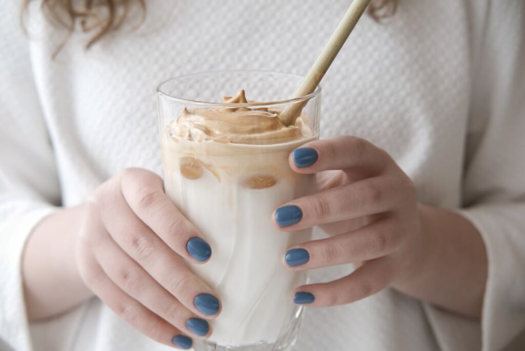 A woman's hands holding a glass of dalgona chocolate.