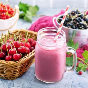 A cherry smoothie in a glass with fresh cherries in the background.