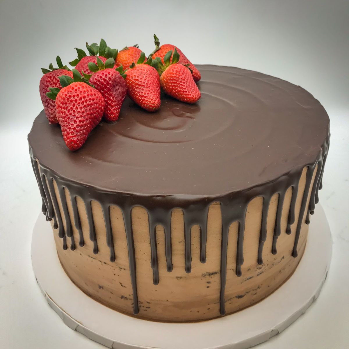 A chocolate cake with a simple chocolate ganache drizzle topped with fresh strawberries.