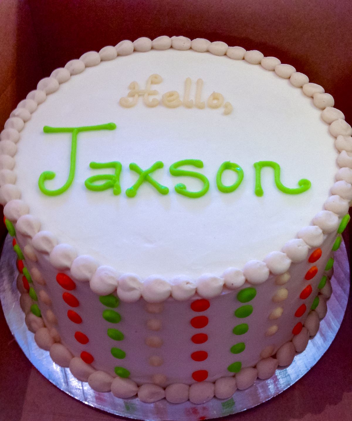 A smooth white cake with buttercream dots on the sides and a message of "Hello, jackson" on top of the cake.
