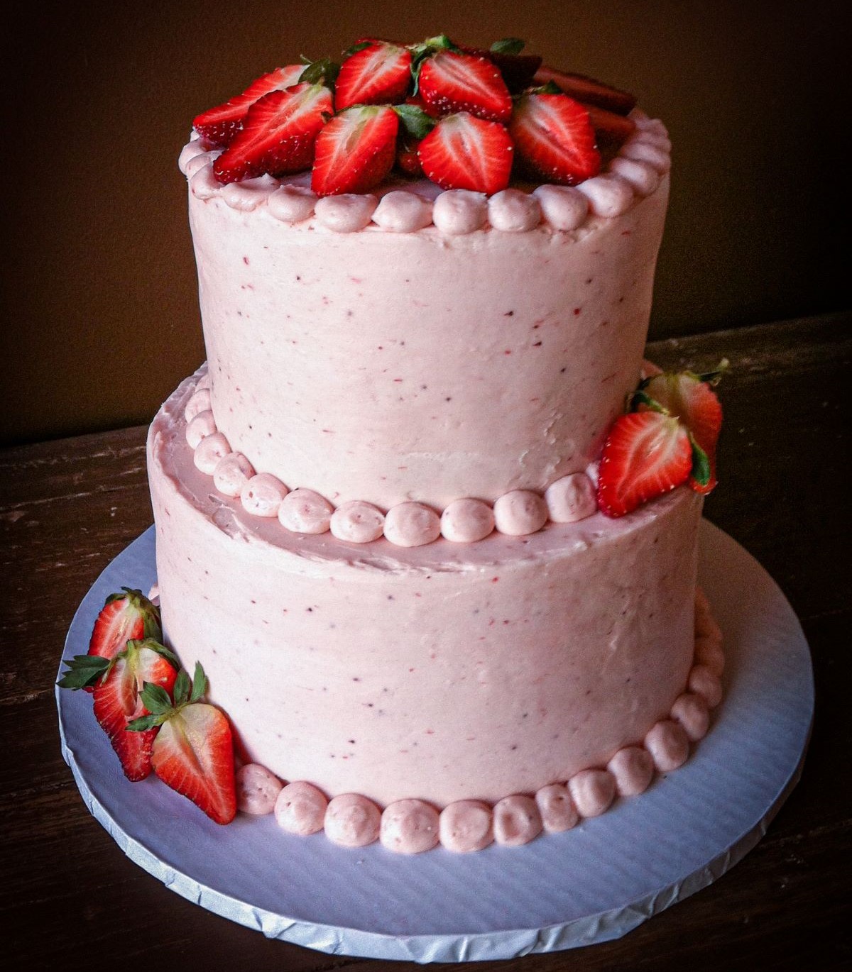 A smooth simple tiered cake with strawberry buttercream and fresh berries.