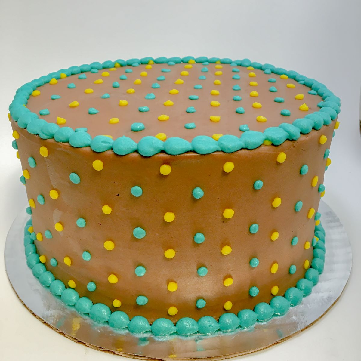 A chocolate buttercream minimalist cake with a simple yellow and teal dot design.
